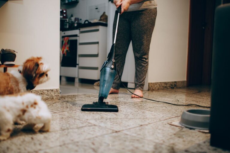 Cleaner vacuuming a kitchen floor while the family dog watches